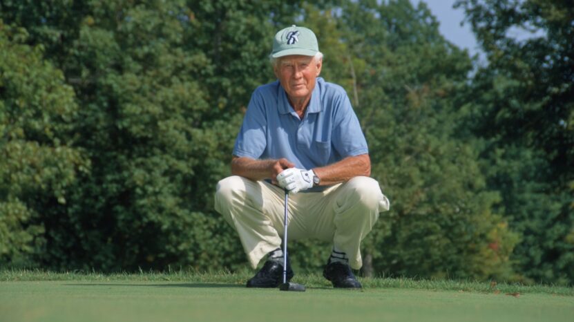Elderly man crouching on a golf course, focused and holding a club, surrounded by trees