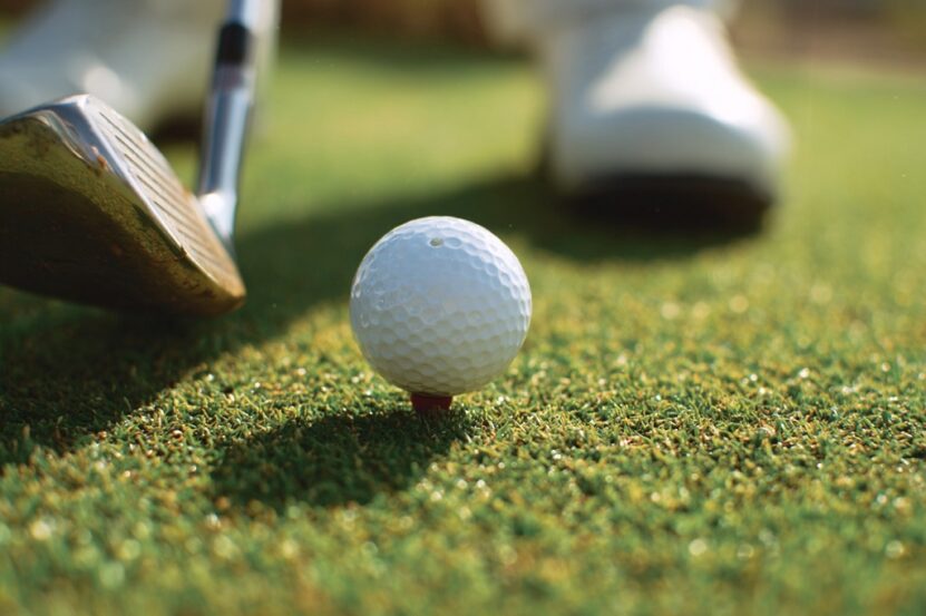 Golf ball on tee in front of club and golfer’s feet